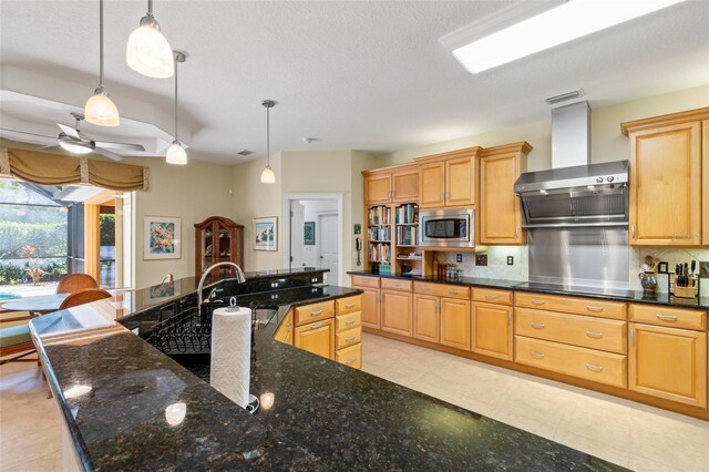 kitchen featuring backsplash, sink, ceiling fan, wall chimney range hood, and stainless steel microwave