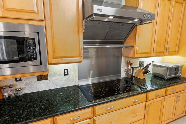 kitchen with dark stone countertops, stainless steel microwave, black electric cooktop, and ventilation hood