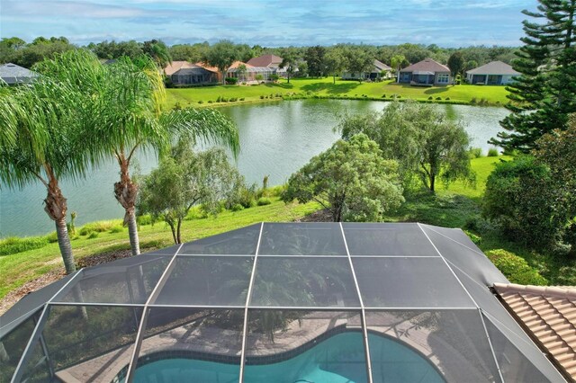 view of swimming pool with glass enclosure, a lawn, and a water view