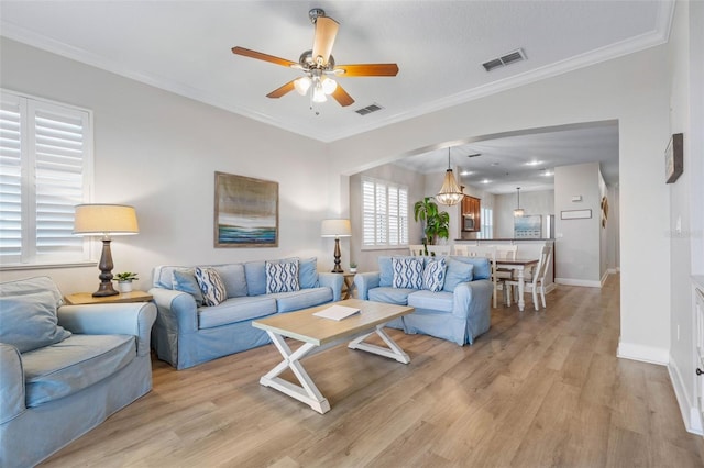 living room with ceiling fan with notable chandelier, light hardwood / wood-style floors, and crown molding