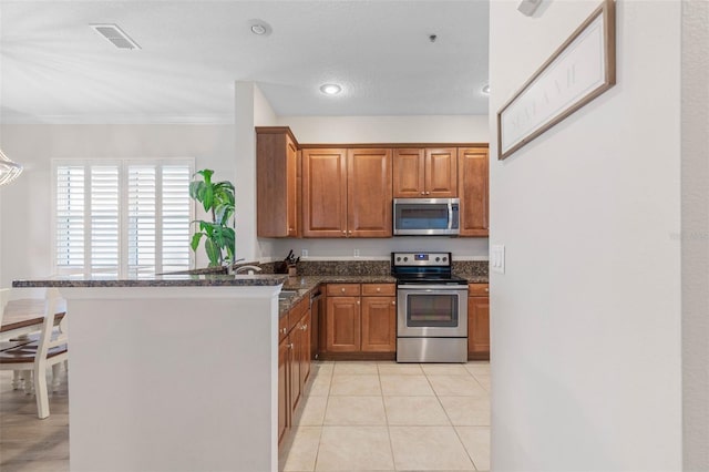 kitchen featuring light tile patterned flooring, kitchen peninsula, a textured ceiling, appliances with stainless steel finishes, and dark stone countertops