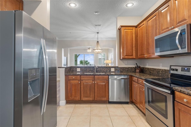 kitchen with appliances with stainless steel finishes, a textured ceiling, dark stone countertops, and sink