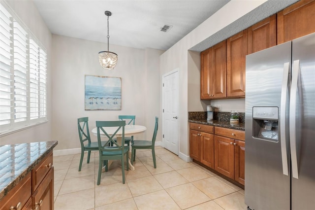 kitchen with dark stone countertops, light tile patterned floors, pendant lighting, an inviting chandelier, and stainless steel fridge with ice dispenser