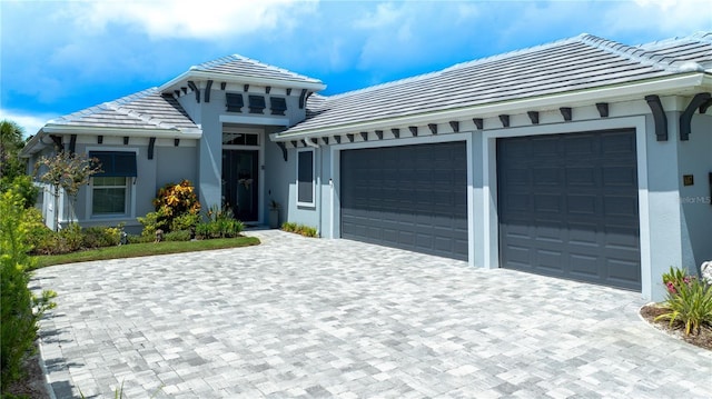 view of front of house with stucco siding, a tile roof, decorative driveway, and an attached garage