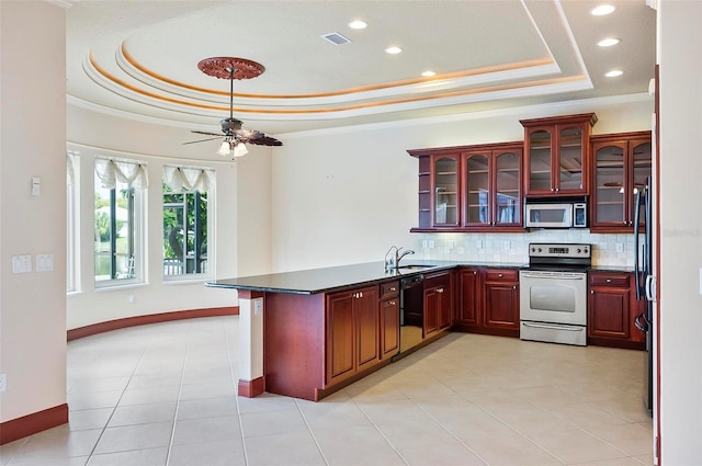 kitchen featuring kitchen peninsula, ceiling fan, decorative backsplash, a tray ceiling, and appliances with stainless steel finishes