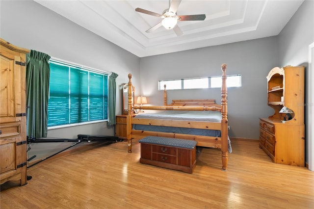 bedroom featuring ceiling fan, light wood-type flooring, and a tray ceiling