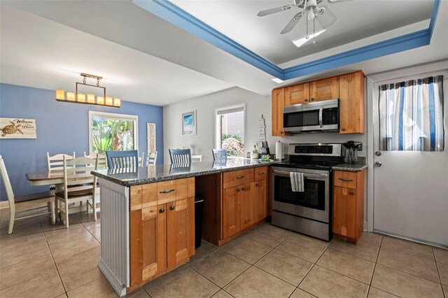 kitchen featuring appliances with stainless steel finishes, dark stone counters, kitchen peninsula, and ceiling fan