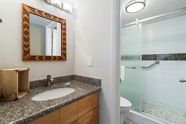 bathroom featuring a shower with door, vanity, and toilet