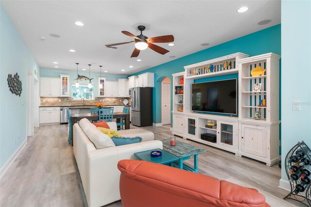 living room featuring ceiling fan, sink, a textured ceiling, and light hardwood / wood-style flooring