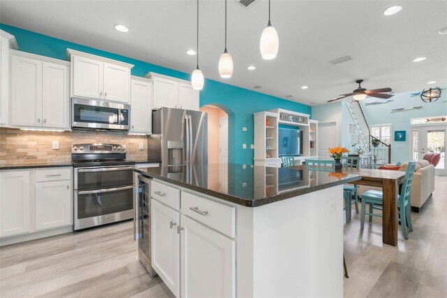 kitchen featuring white cabinets, decorative light fixtures, appliances with stainless steel finishes, ceiling fan, and a kitchen island