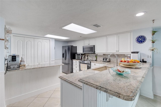 kitchen with light stone countertops, stainless steel appliances, sink, kitchen peninsula, and a breakfast bar