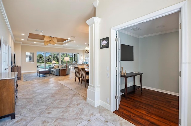 corridor featuring ornamental molding, light hardwood / wood-style flooring, ornate columns, and a tray ceiling