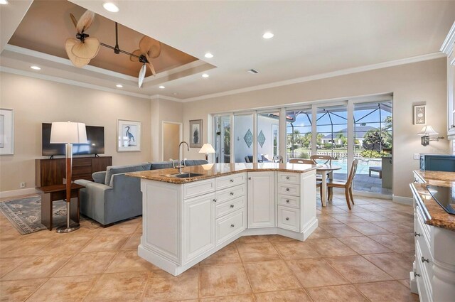 kitchen featuring a kitchen island with sink, crown molding, sink, a tray ceiling, and white cabinets