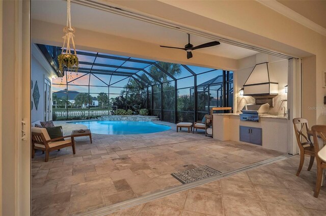 pool at dusk with an outdoor kitchen, ceiling fan, a patio, grilling area, and glass enclosure