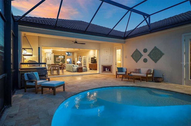 pool at dusk with a lanai, a patio area, an outdoor hangout area, exterior kitchen, and ceiling fan