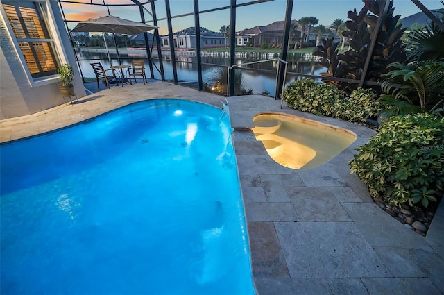 pool at dusk featuring glass enclosure, a patio, a water view, and pool water feature