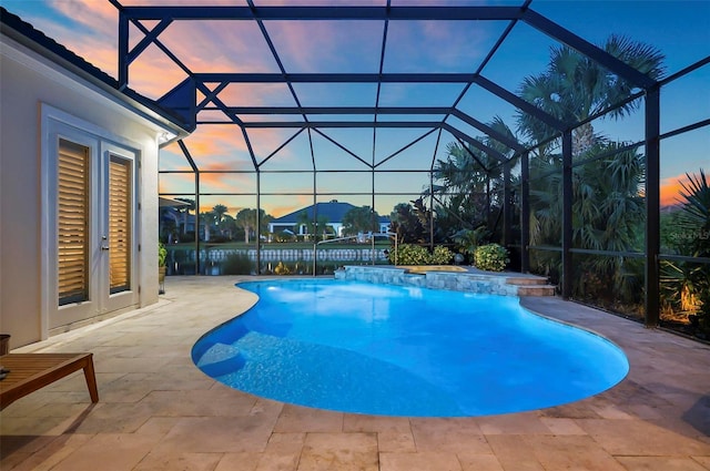 pool at dusk featuring glass enclosure, pool water feature, and a patio