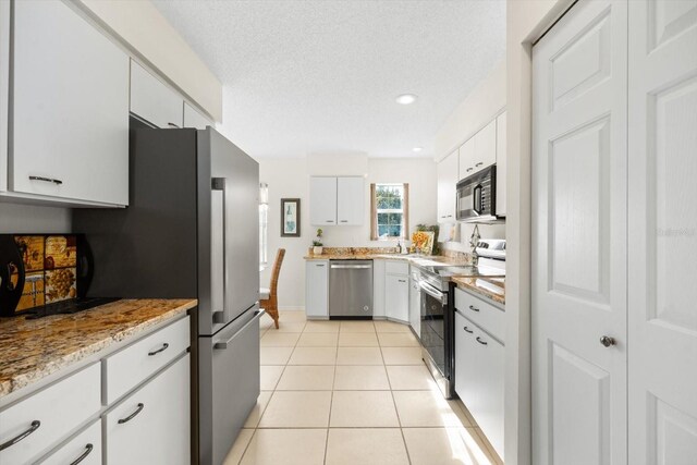 kitchen with a textured ceiling, light tile patterned floors, appliances with stainless steel finishes, and white cabinetry