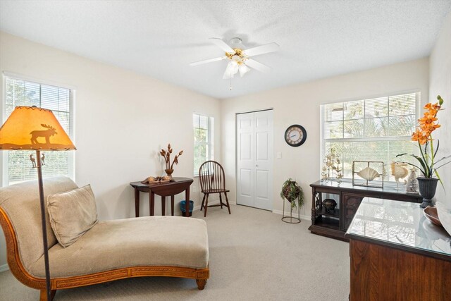 living area with ceiling fan, a wealth of natural light, a textured ceiling, and light colored carpet