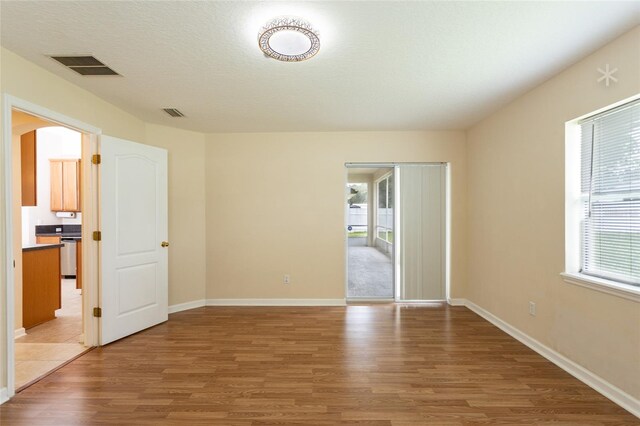 empty room with a textured ceiling, a healthy amount of sunlight, and wood-type flooring