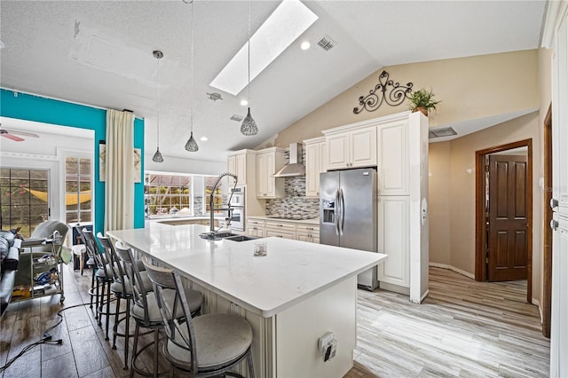 kitchen with hanging light fixtures, light wood-type flooring, stainless steel fridge, an island with sink, and ceiling fan