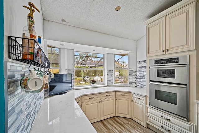 kitchen featuring stainless steel double oven, a textured ceiling, backsplash, light stone countertops, and cream cabinets