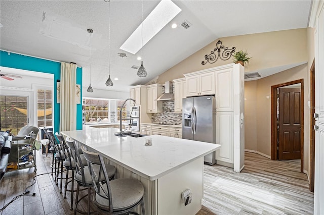 kitchen with light hardwood / wood-style floors, stainless steel refrigerator with ice dispenser, ceiling fan, a kitchen bar, and a center island with sink