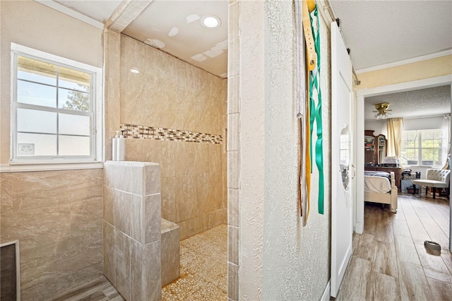 bathroom with crown molding, a tile shower, wood-type flooring, and a textured ceiling