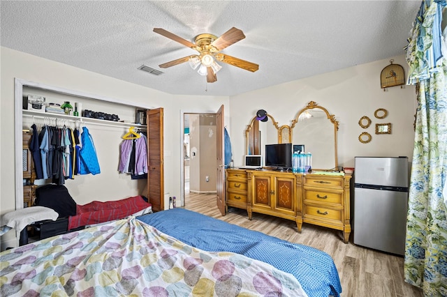 bedroom featuring a textured ceiling, ceiling fan, hardwood / wood-style floors, and stainless steel fridge