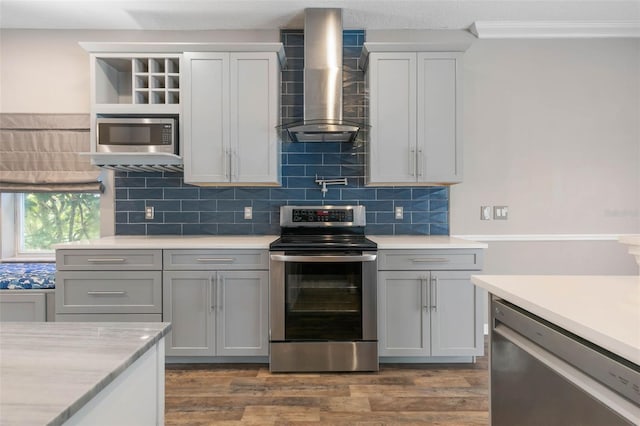 kitchen with gray cabinetry, stainless steel appliances, wall chimney range hood, and dark hardwood / wood-style floors