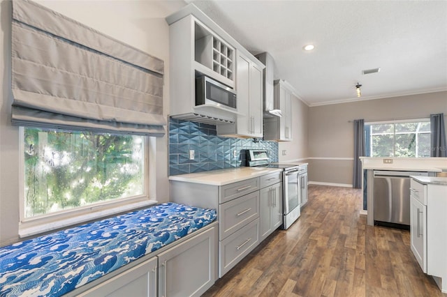 kitchen with decorative backsplash, ornamental molding, gray cabinets, appliances with stainless steel finishes, and dark hardwood / wood-style flooring