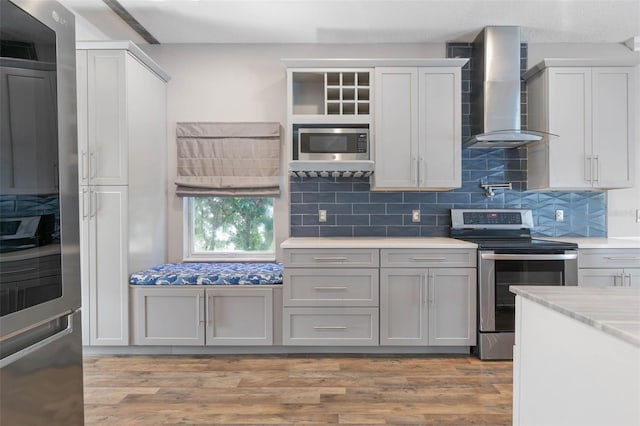 kitchen with stainless steel appliances, wall chimney range hood, light hardwood / wood-style flooring, and tasteful backsplash