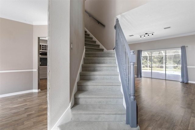 stairway featuring crown molding, hardwood / wood-style floors, and track lighting