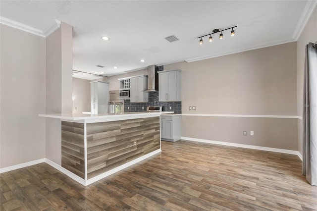 kitchen with ornamental molding, dark wood-type flooring, wall chimney range hood, and stainless steel microwave