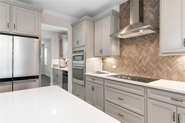 kitchen featuring appliances with stainless steel finishes, crown molding, wall chimney range hood, gray cabinetry, and decorative backsplash