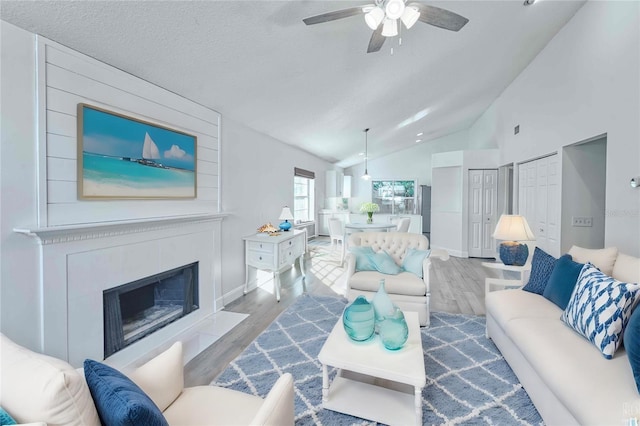 living room featuring vaulted ceiling, ceiling fan, light hardwood / wood-style floors, a textured ceiling, and a large fireplace