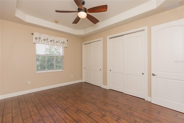 unfurnished bedroom featuring two closets, ceiling fan, a raised ceiling, and dark wood-type flooring