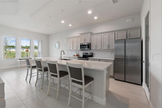 kitchen with a kitchen island with sink, sink, a breakfast bar, appliances with stainless steel finishes, and gray cabinetry