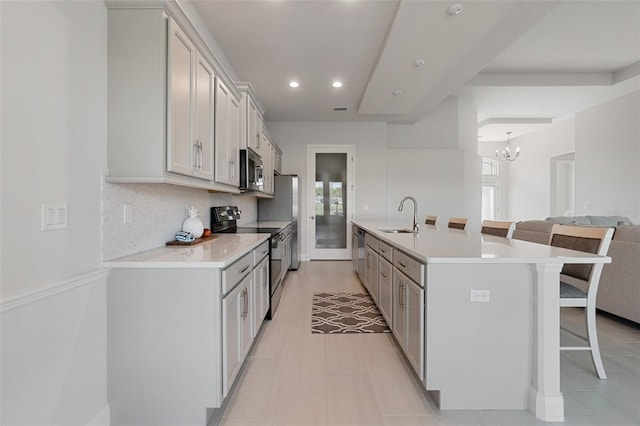 kitchen featuring a kitchen breakfast bar, an inviting chandelier, an island with sink, sink, and appliances with stainless steel finishes