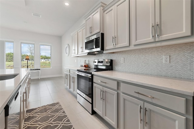 kitchen featuring gray cabinets, light stone countertops, decorative backsplash, appliances with stainless steel finishes, and light tile patterned flooring