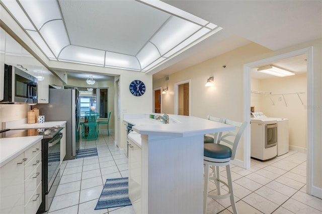 kitchen with white cabinets, light tile patterned floors, stainless steel appliances, independent washer and dryer, and a breakfast bar area