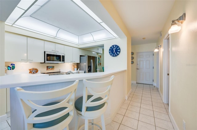 kitchen with appliances with stainless steel finishes, a kitchen breakfast bar, white cabinets, kitchen peninsula, and light tile patterned floors