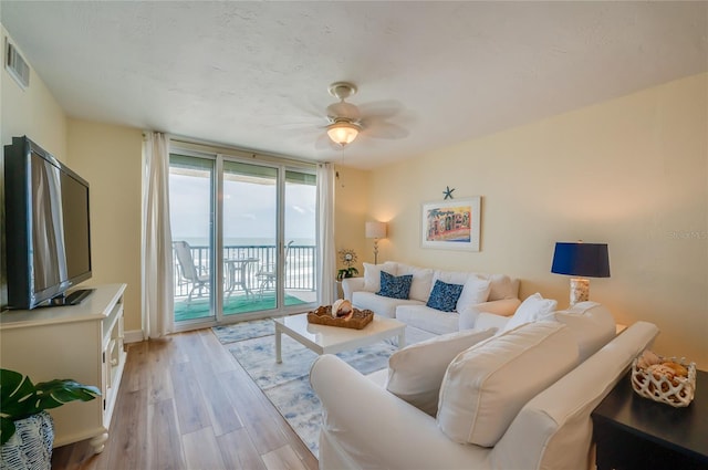 living room featuring ceiling fan, light hardwood / wood-style flooring, floor to ceiling windows, and a water view