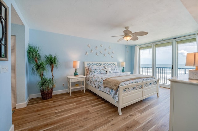 bedroom with access to outside, light hardwood / wood-style flooring, a water view, and ceiling fan