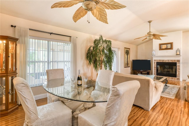 dining room with lofted ceiling, ceiling fan, light wood-type flooring, and a brick fireplace