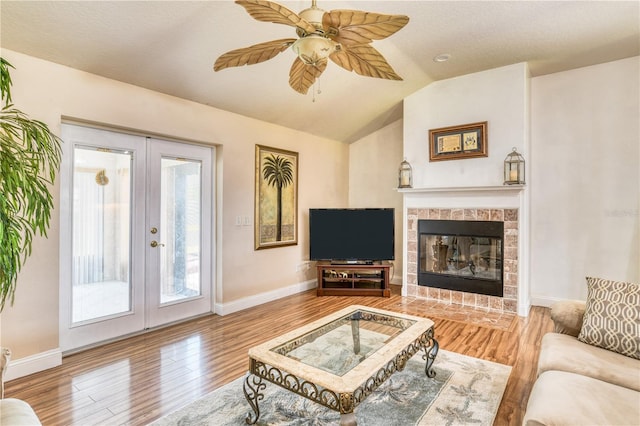 living room featuring light wood-type flooring, vaulted ceiling, a tiled fireplace, and ceiling fan