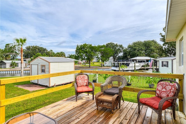 deck with a boat dock, a storage unit, a water view, and a yard