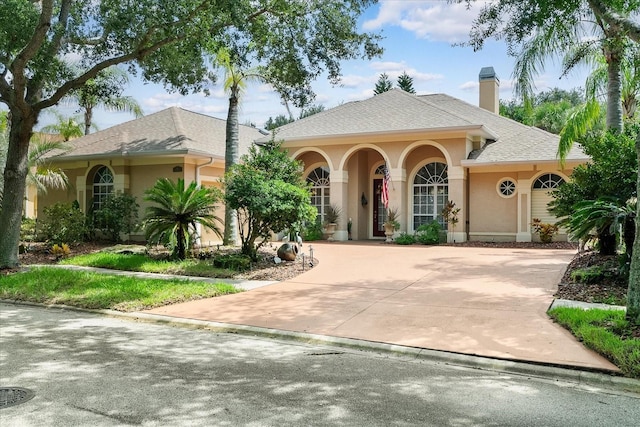 view of front of home with stucco siding, a chimney, driveway, and a shingled roof