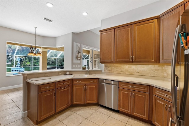 kitchen featuring a sink, stainless steel appliances, a peninsula, brown cabinetry, and light countertops