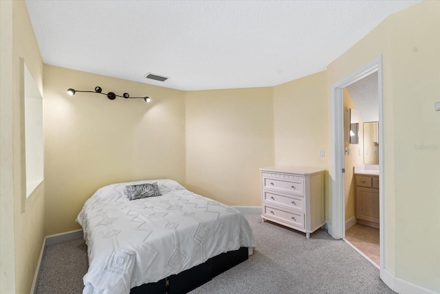 bedroom featuring visible vents, light colored carpet, ensuite bath, and baseboards